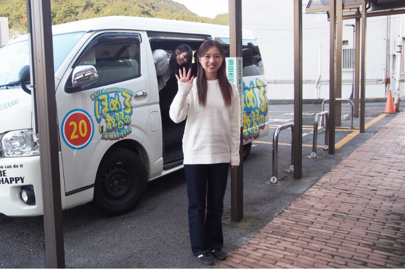 海田自動車学校の送迎車の前で手を振る在校生の写真