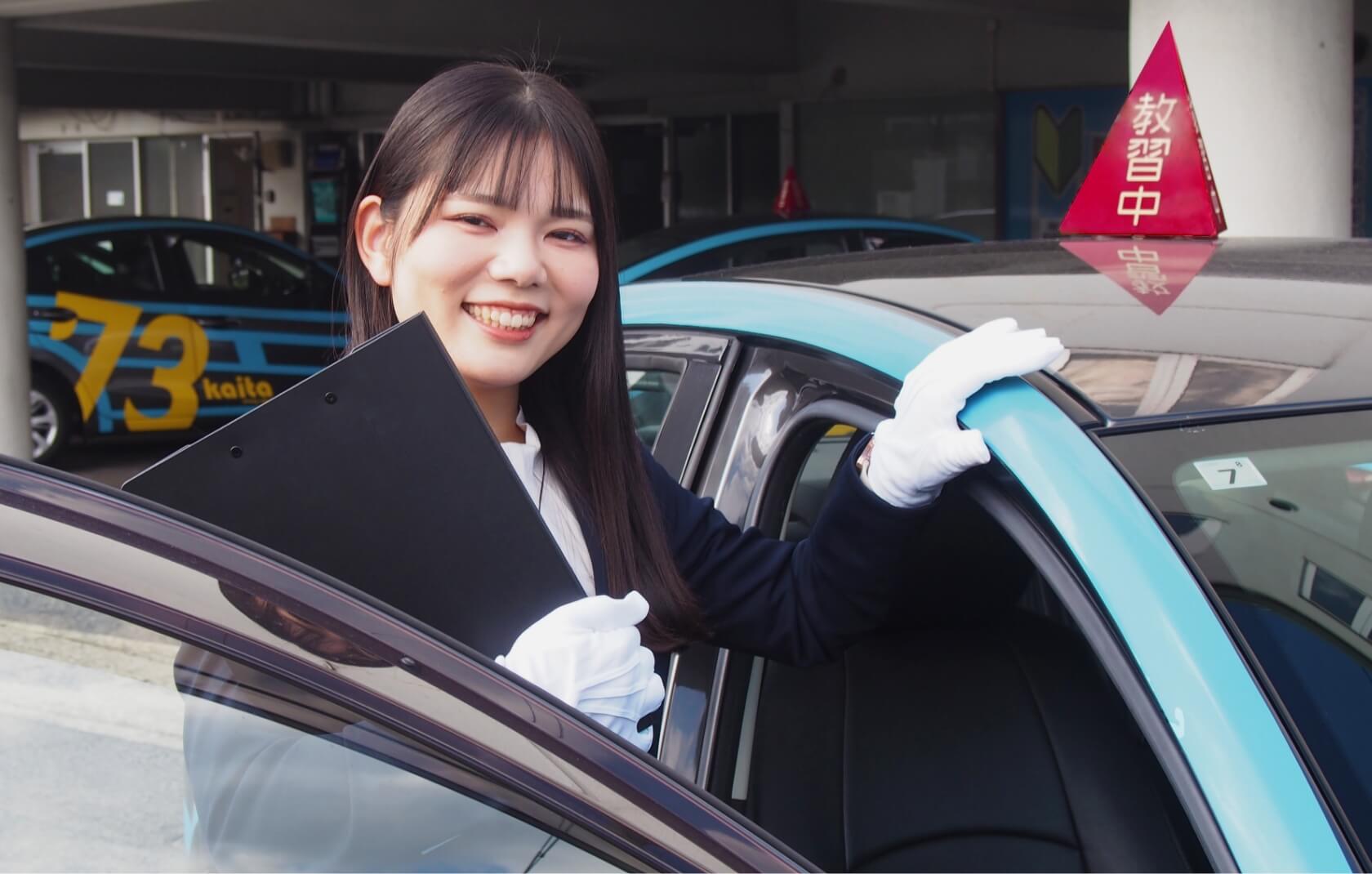 教習車に手を添えて笑顔を見せる講師の写真