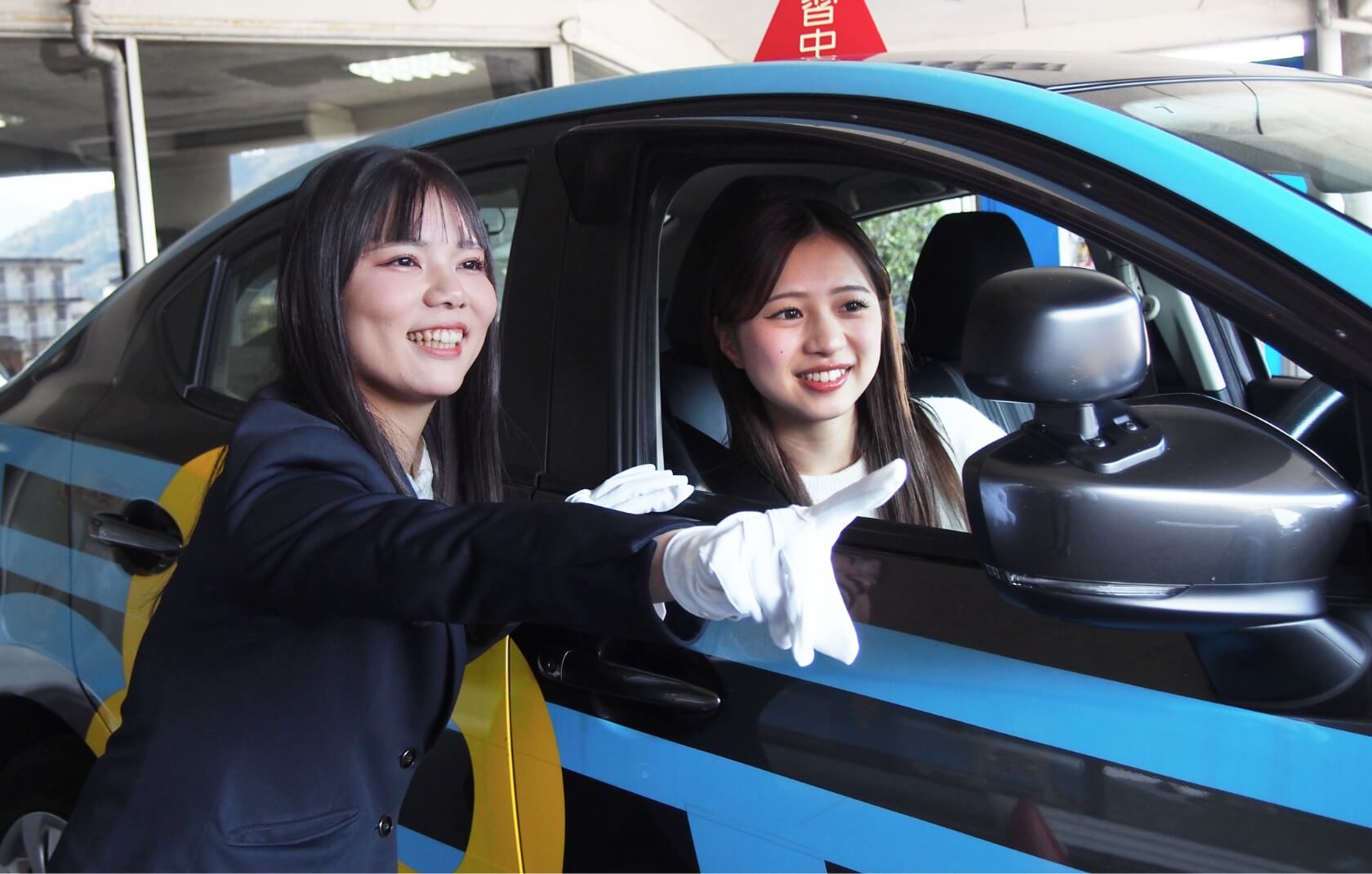 教習車の外で指導をする講師と、教習車の運転席に座っている在校生