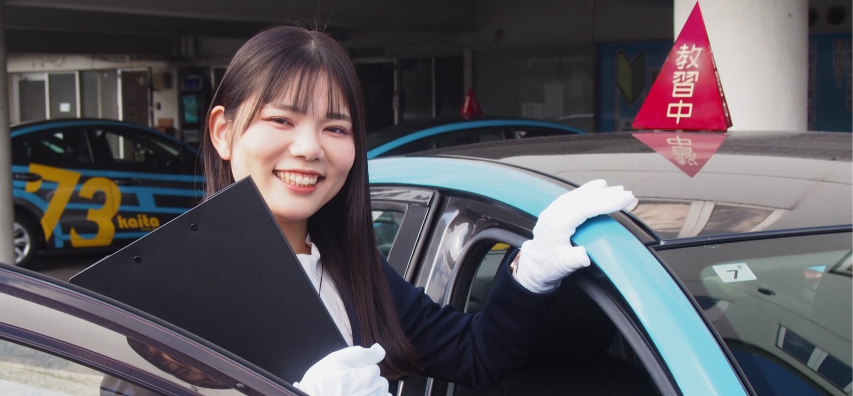 教習車に手を添えて笑顔を見せる講師の写真