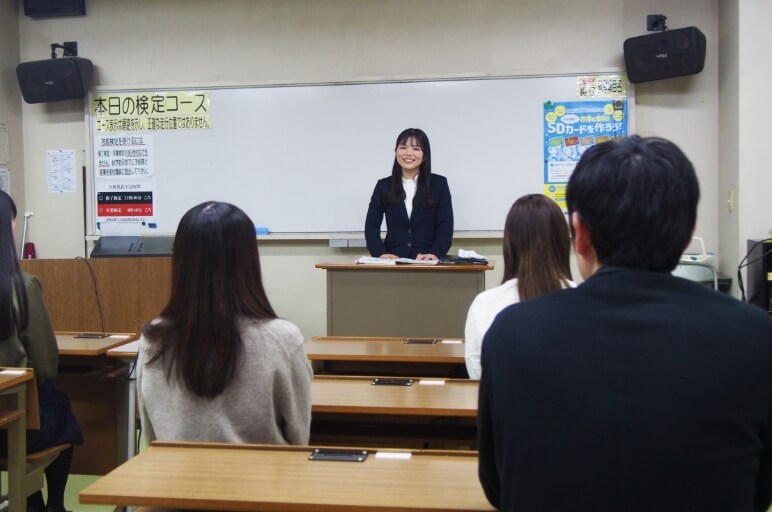 教室の前方に立ってで授業をしている講師と、授業を受けている在校生の後ろ姿