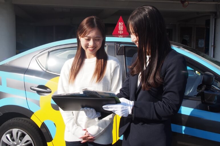 教習車の外で講師から説明を受けている在校生の写真